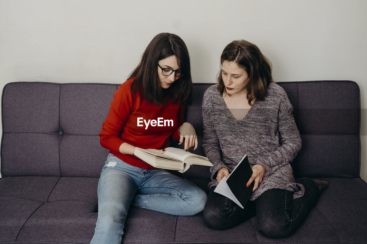 Young females holding book sitting on sofa at home