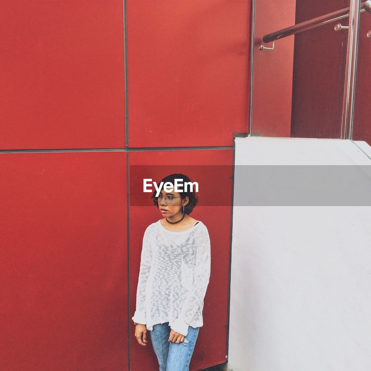 Woman looking away while standing by red wall