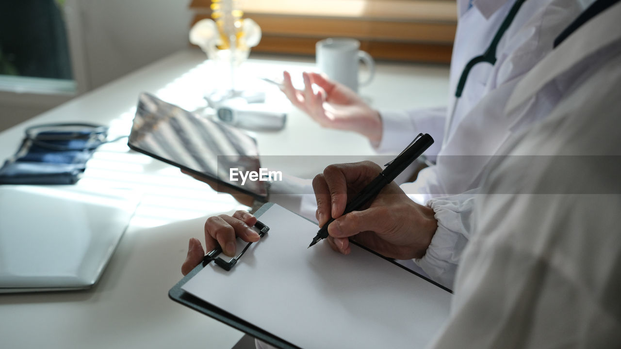 midsection of doctor writing in book at table