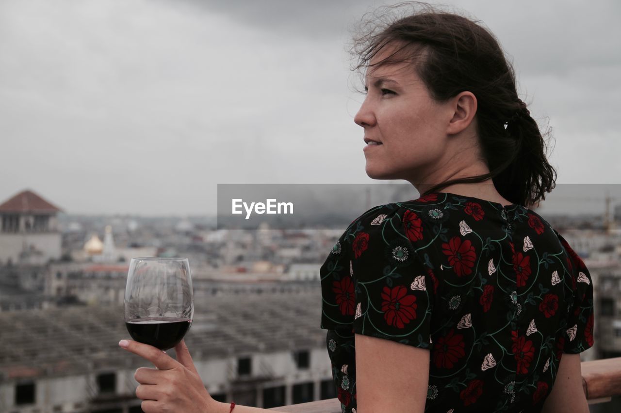 Young woman holding wineglass against sky