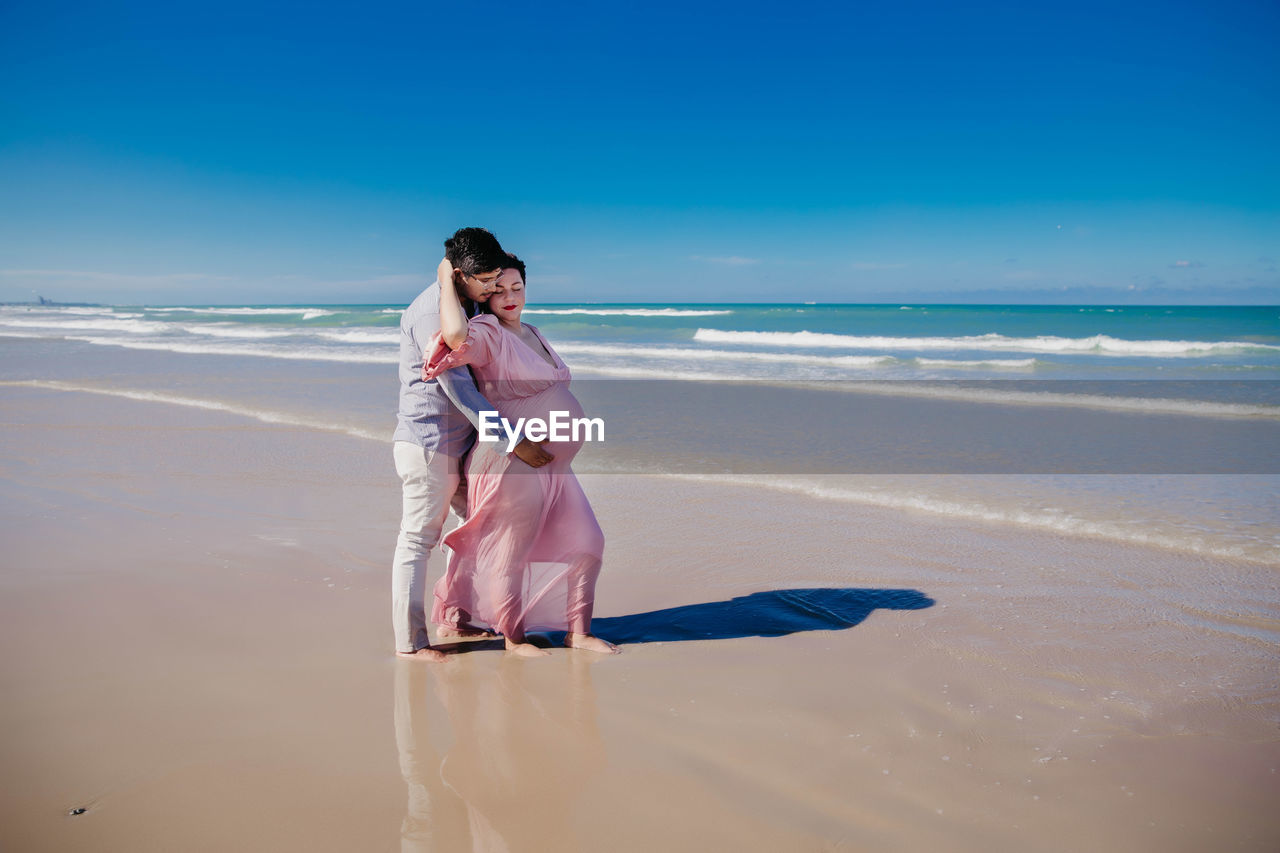 FULL LENGTH OF WOMAN STANDING ON BEACH AGAINST SKY