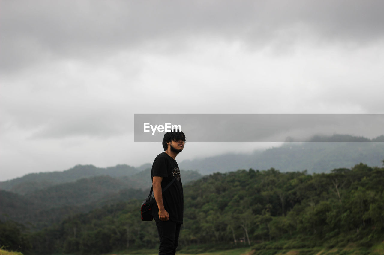 Side view of man standing on against cloudy sky