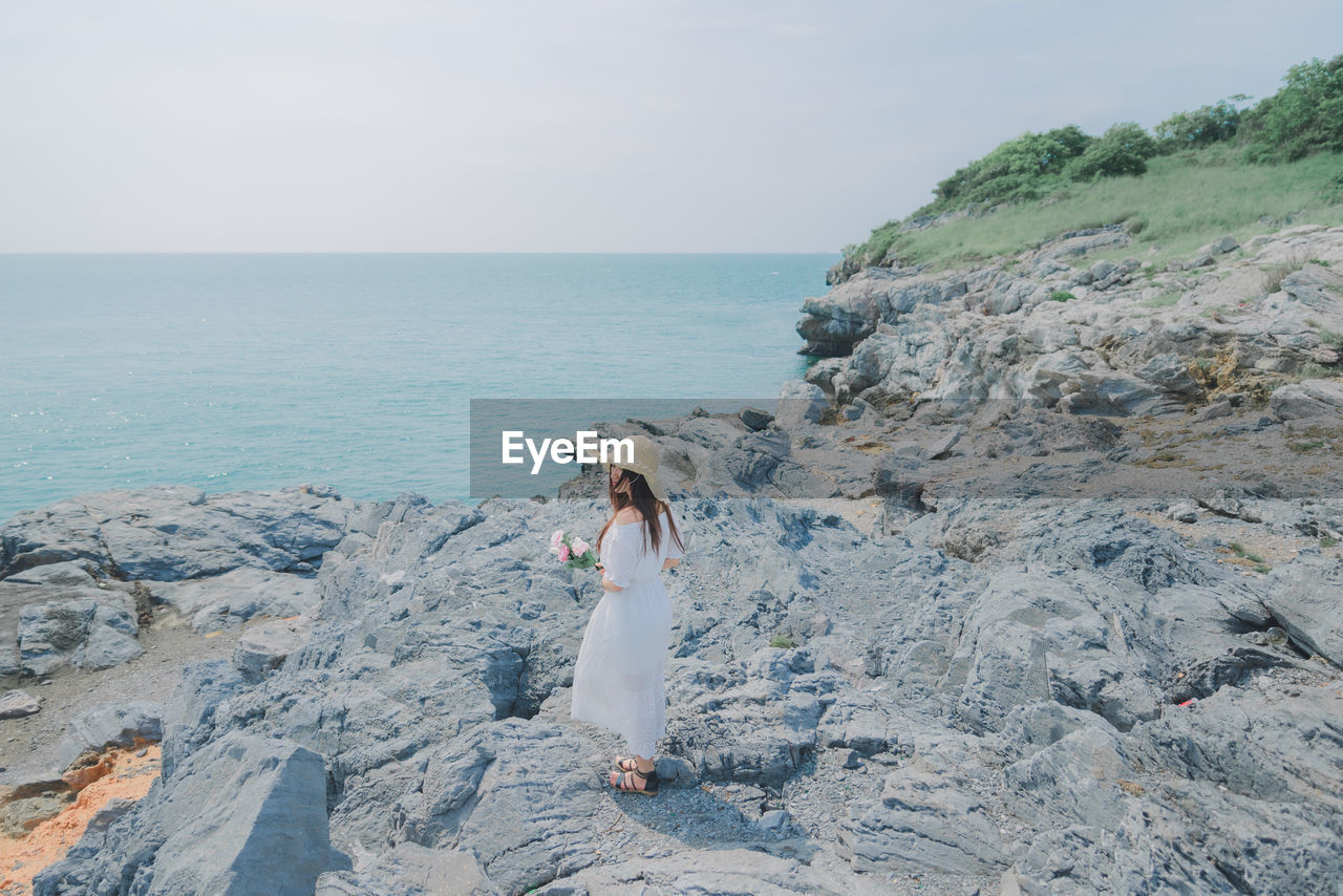 Full length of woman standing on rock by sea against sky