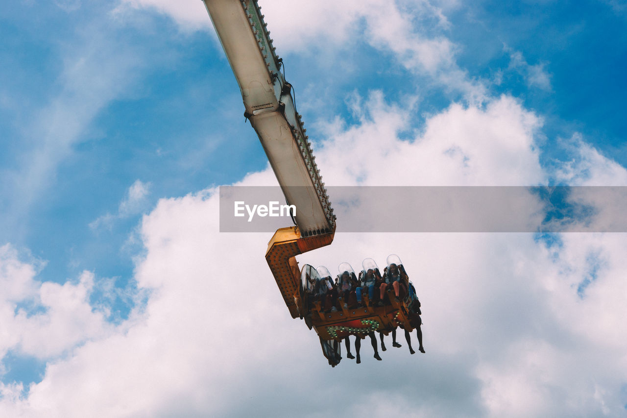 Low angle view of people enjoying suspended ride at amusement park against cloudy sky