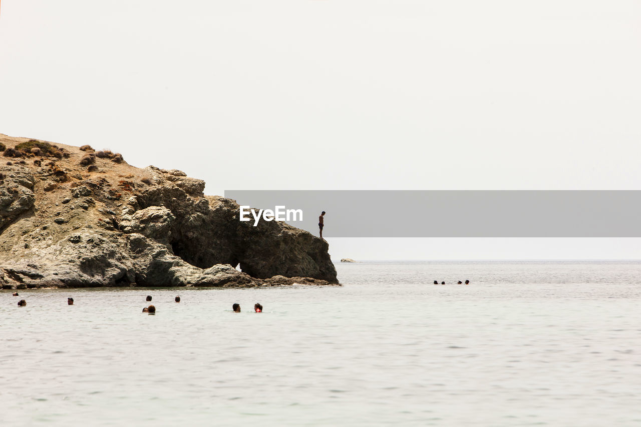 Man standing on rock formation by sea against clear sky during sunny day