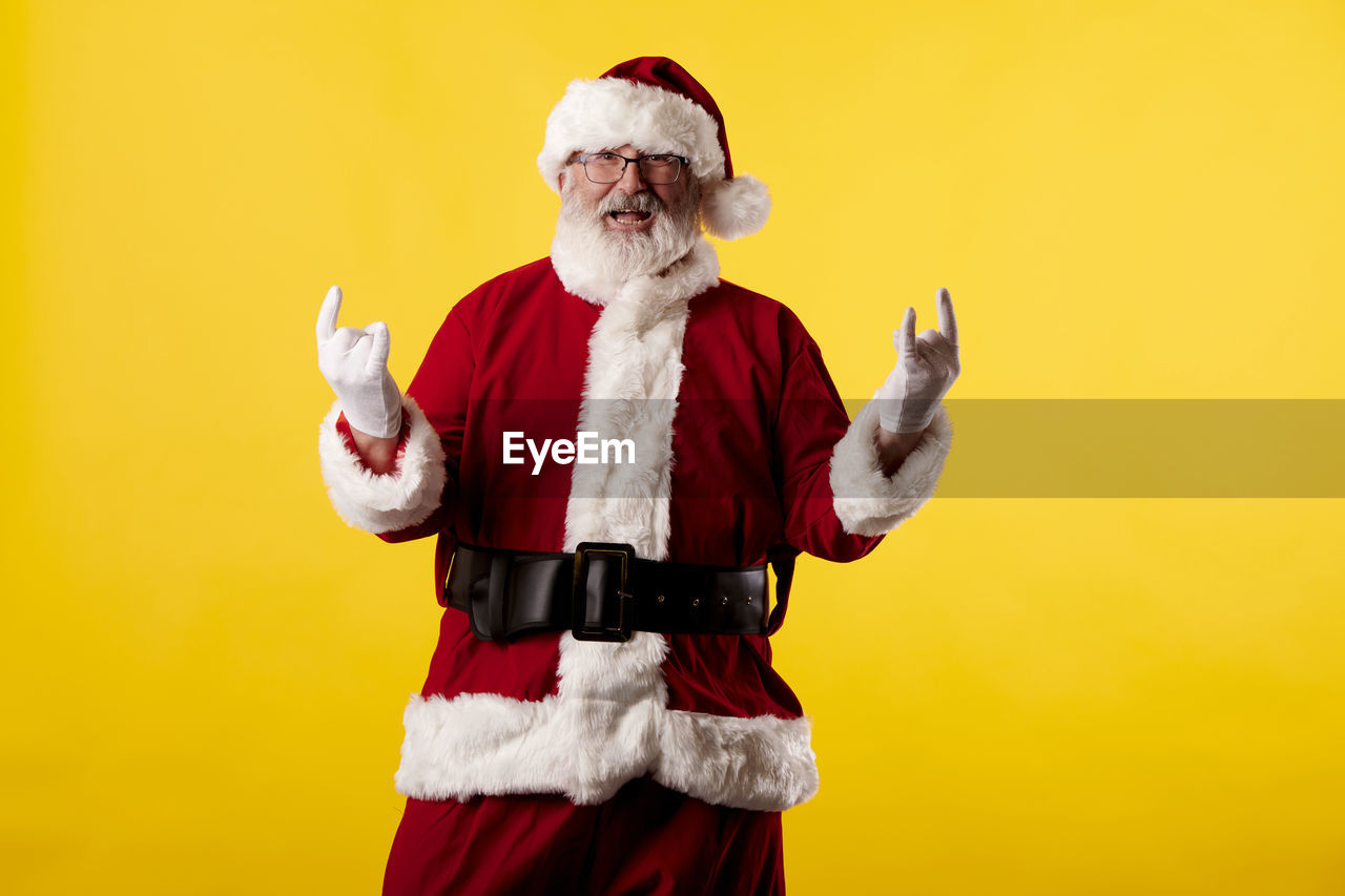 Santa claus making a rocker gesture on yellow background