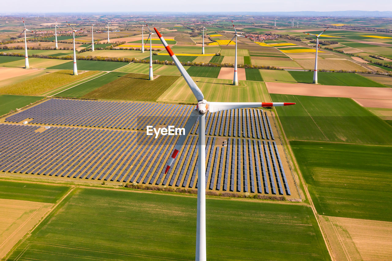 Huge wind turbines between agricultural land and a solar park in rural area from a drone perspective