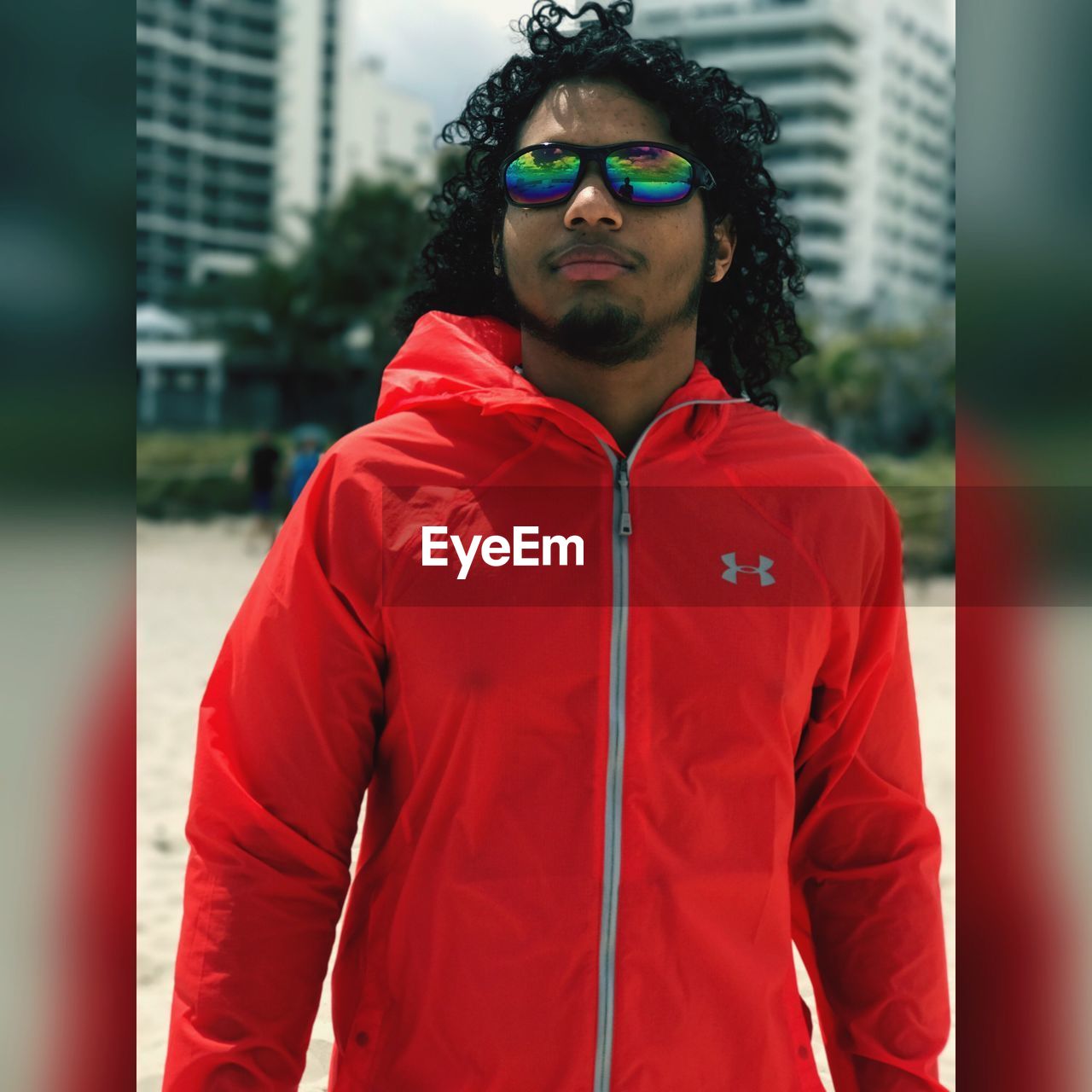 YOUNG MAN WEARING SUNGLASSES STANDING AGAINST CITY IN BACKGROUND