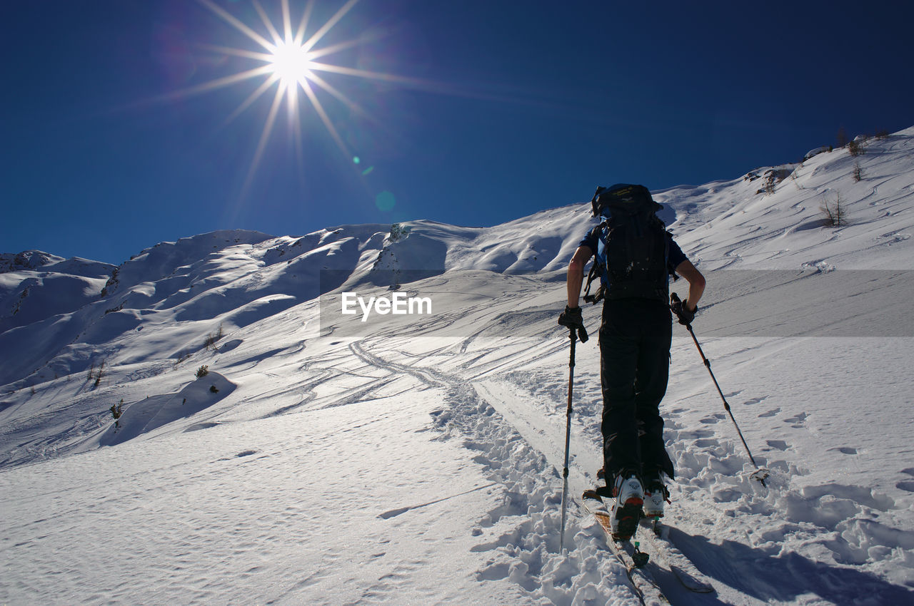 Low angle view of hiker walking on snow covered mountain against bright sky
