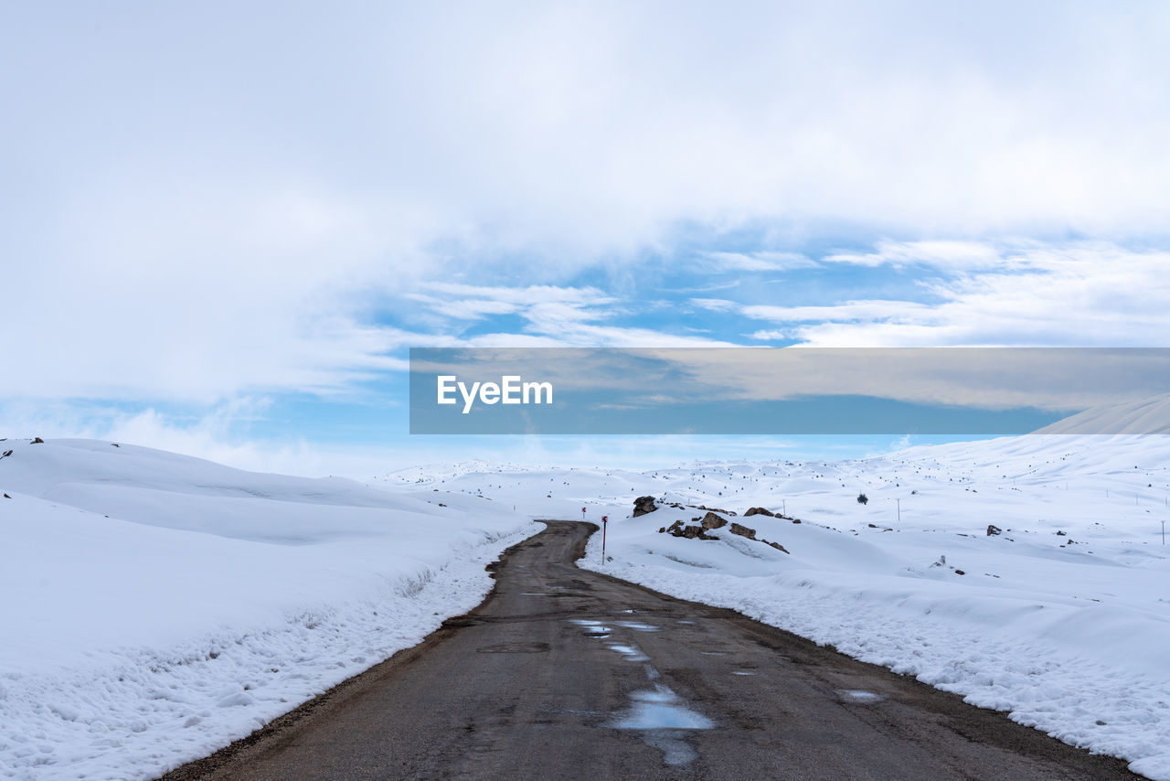 Road on snow covered land against sky