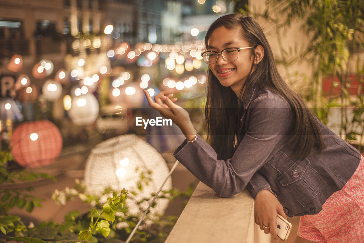 Smiling teenage girl leaning on wall at balcony during night