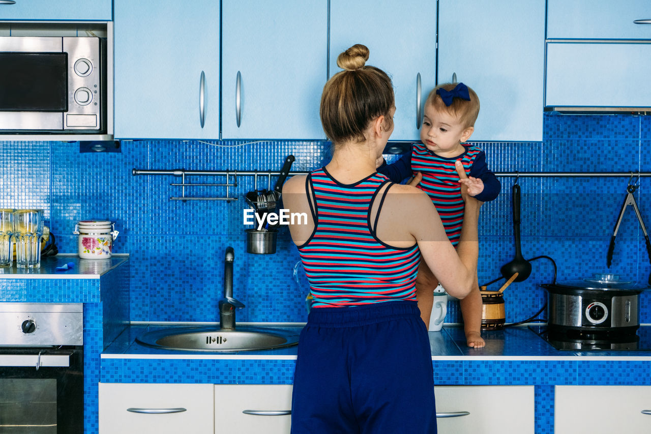 Young mother holding cute baby daughter in kitchen. happy family mother and baby toddler girl