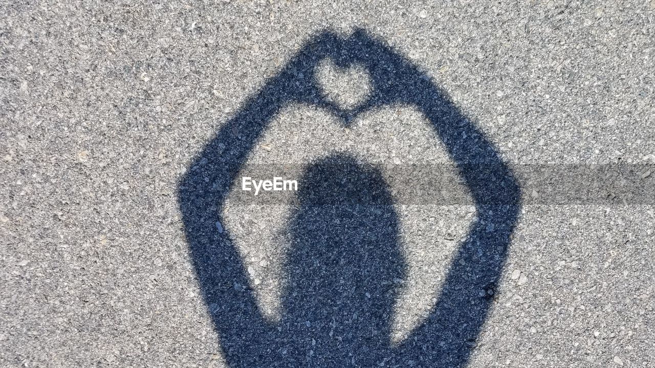 Shadow of person making heart shape on road in city