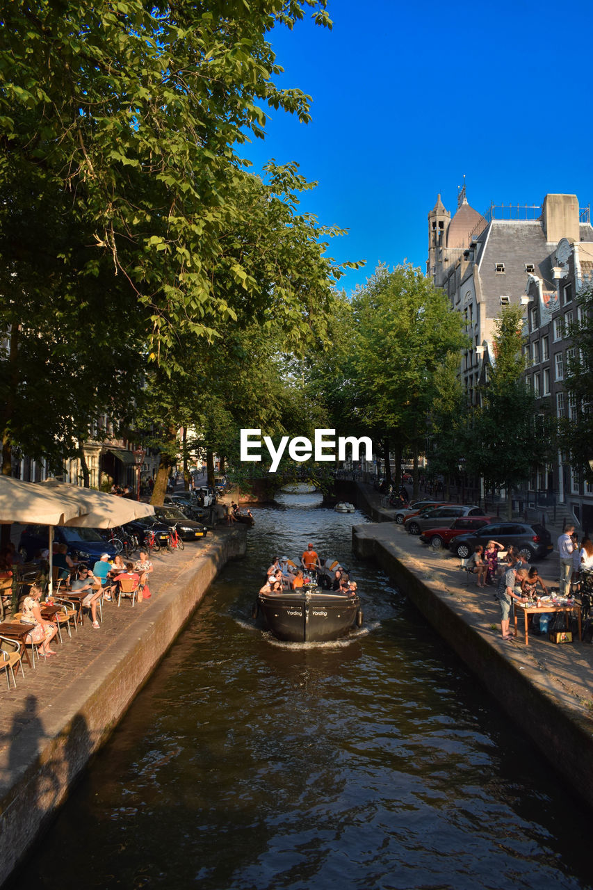 PEOPLE ON BOATS IN CANAL ALONG CITY