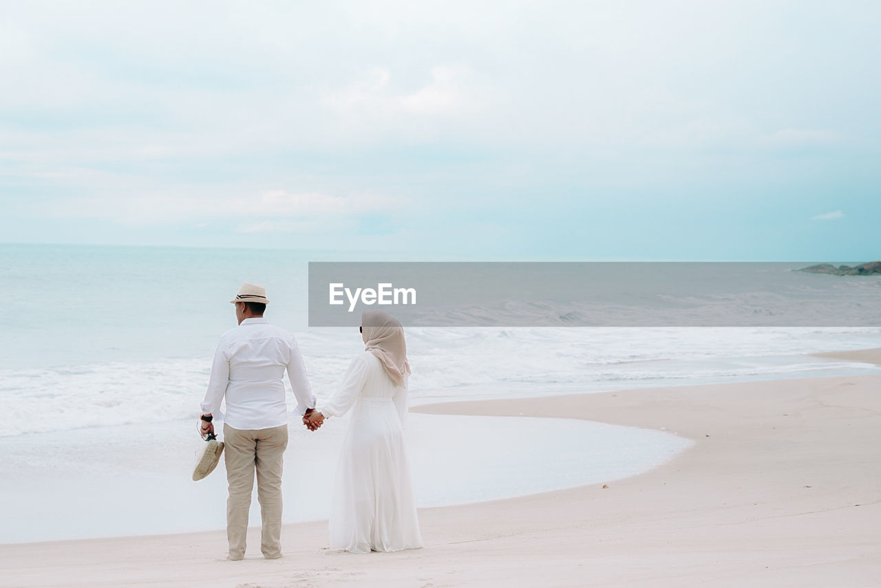 Rear view of woman standing at beach against sky