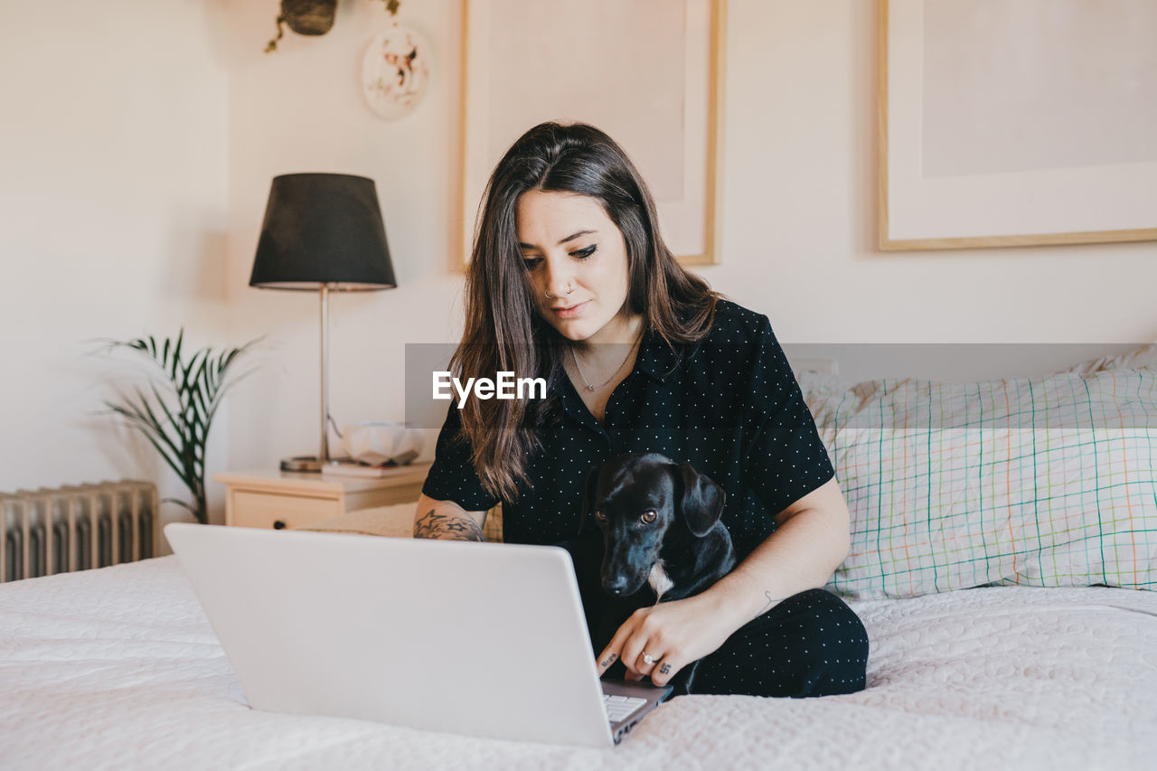 Young woman on the computer in cozy bedroom at home with dog