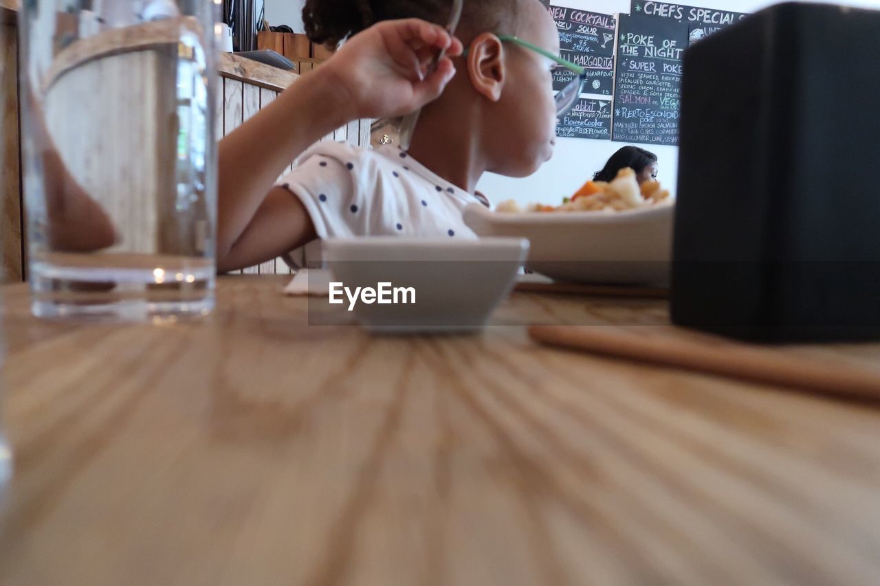 MIDSECTION OF WOMAN USING MOBILE PHONE WHILE SITTING AT TABLE