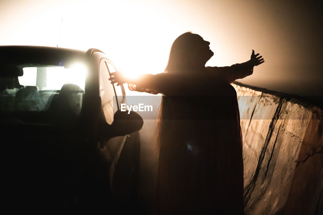 SILHOUETTE PEOPLE STANDING BY CAR AGAINST SKY