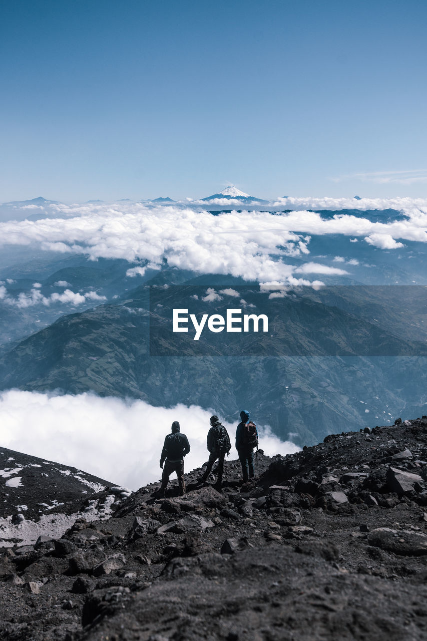 Rear view of male friends standing on cliff against sky