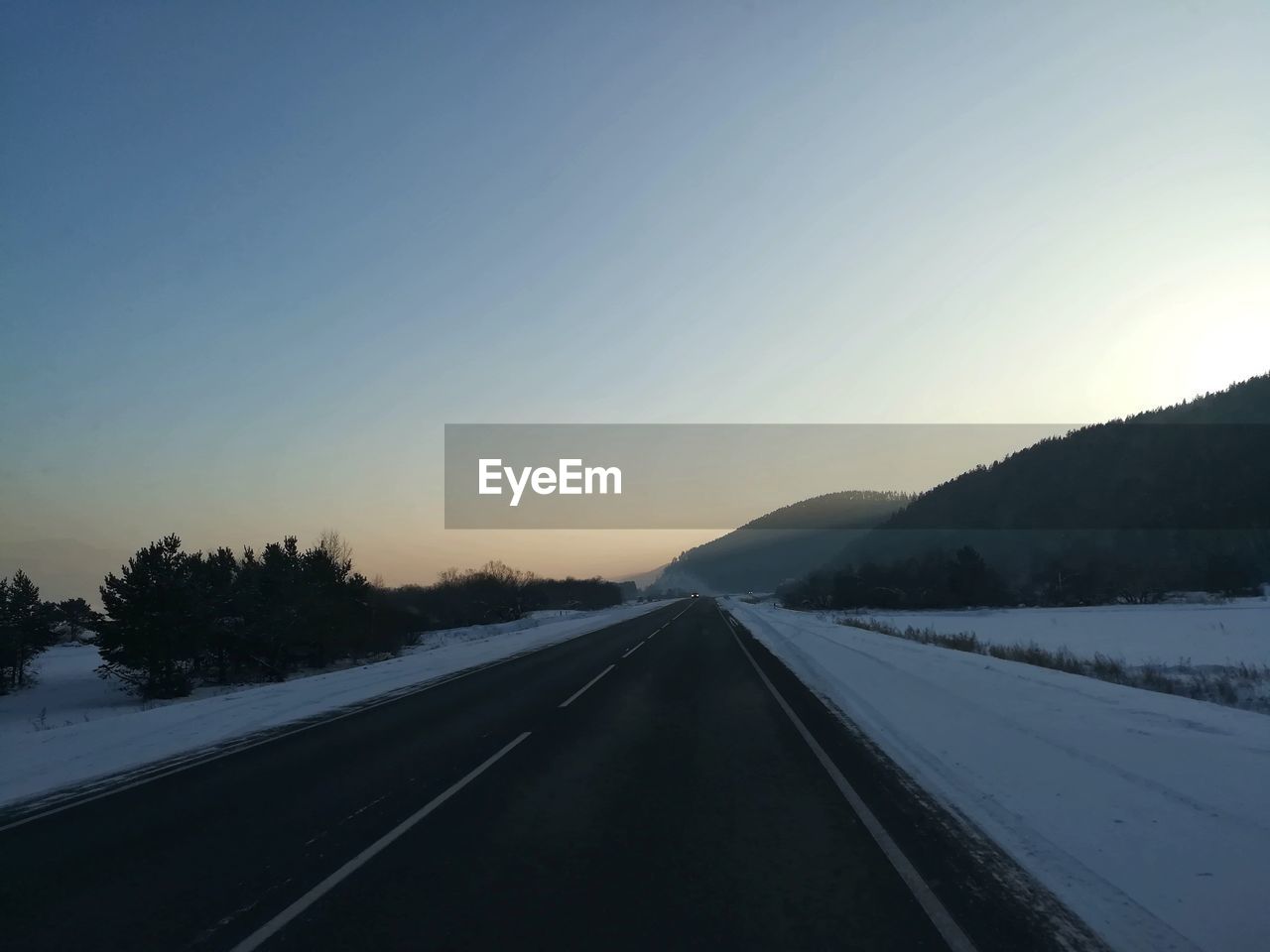 Road amidst trees against clear sky during winter