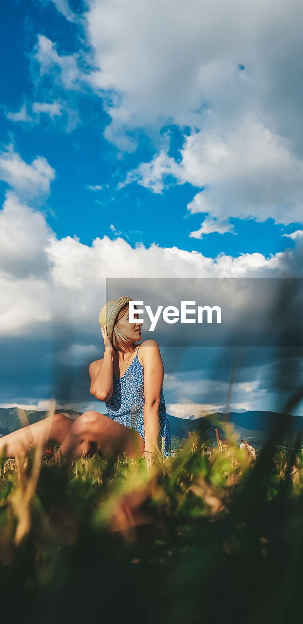 Woman siting by in grassland against sky