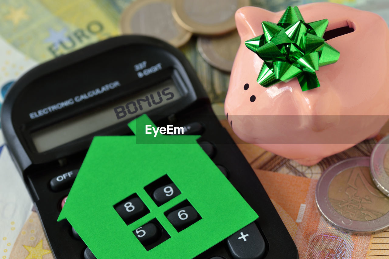 High angle view of paper house over calculator by piggy bank on table