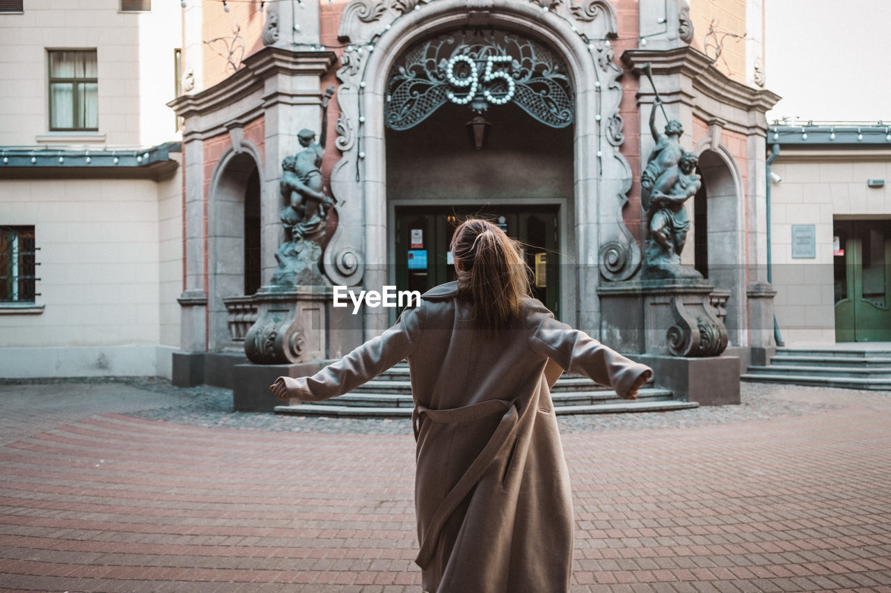 REAR VIEW OF WOMAN STANDING AGAINST BUILDING