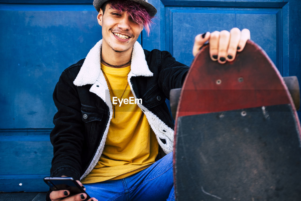 Portrait of young man holding skateboard sitting outdoors