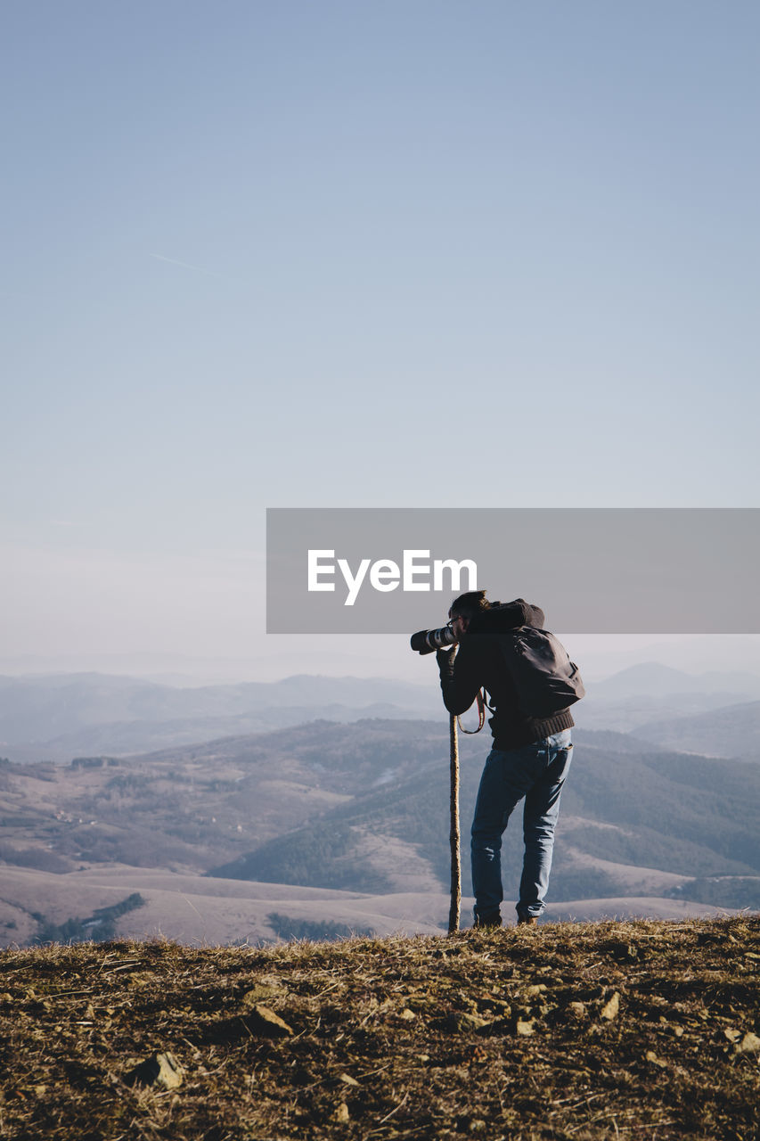 Rear view of man photographing from mountain against clear sky