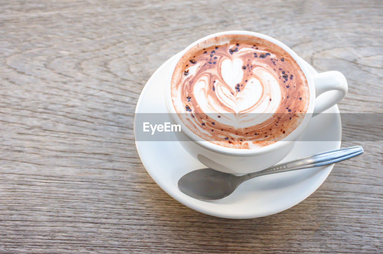 Top view hot coffee espresso topped with a heart shaped milk in white glass on wooden table.