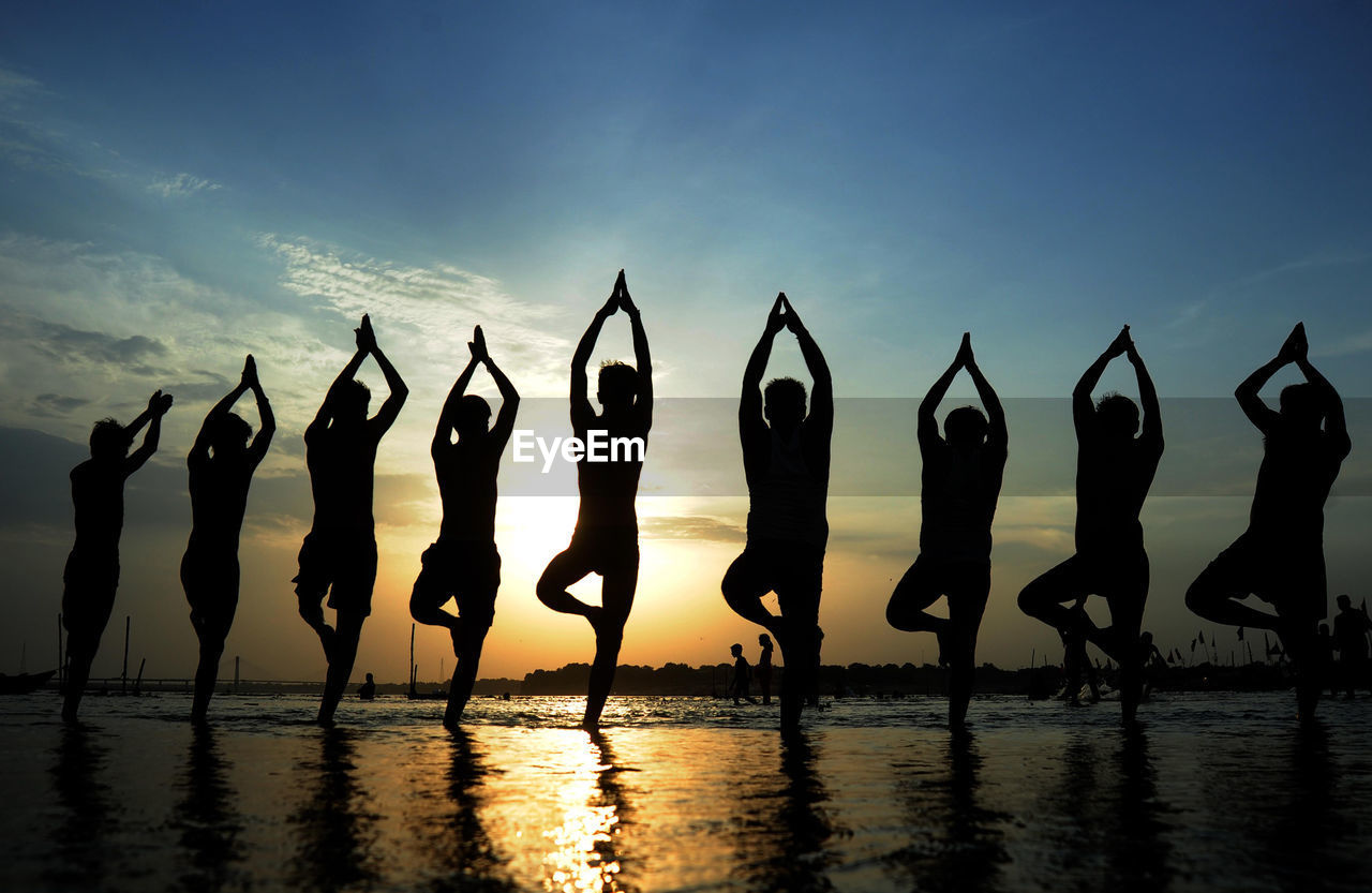 People doing yoga at beach against sky