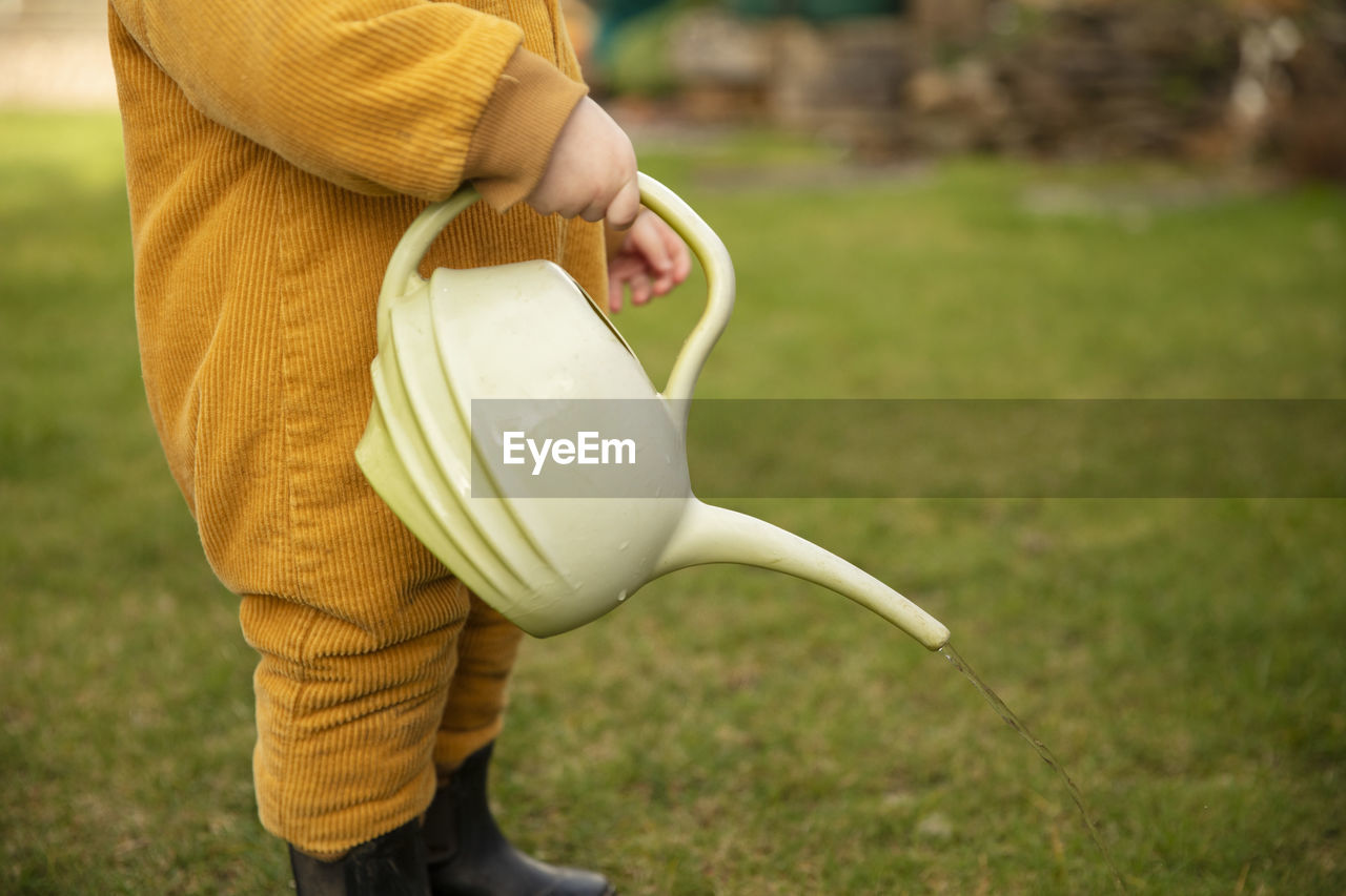 Midsection of boy holding watering can while standing on field