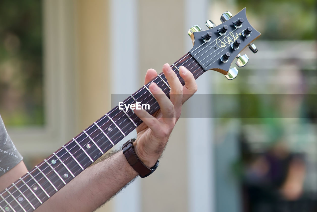 MIDSECTION OF PERSON PLAYING GUITAR AGAINST BLURRED BACKGROUND