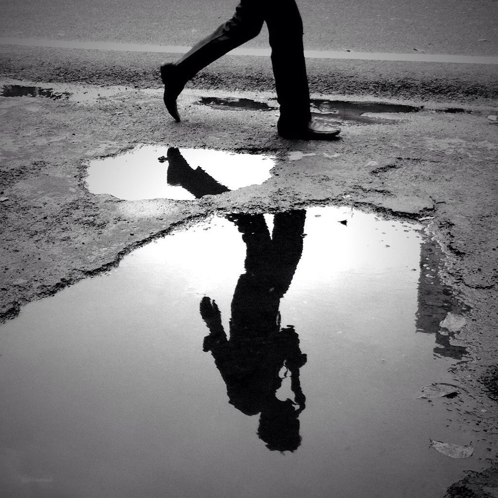 Reflection of man in puddle while walking roadside
