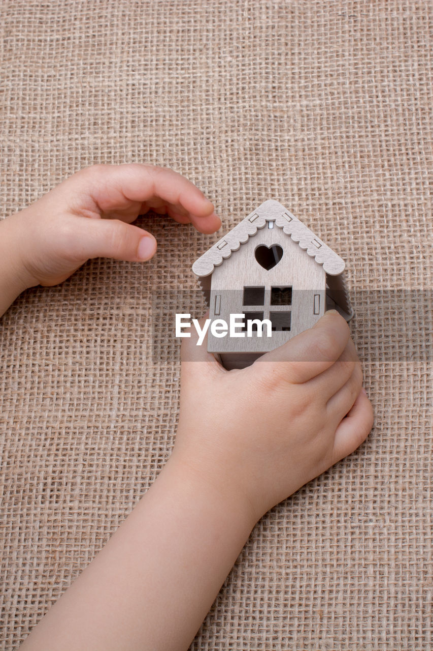 Cropped hand of kid holding model home on burlap