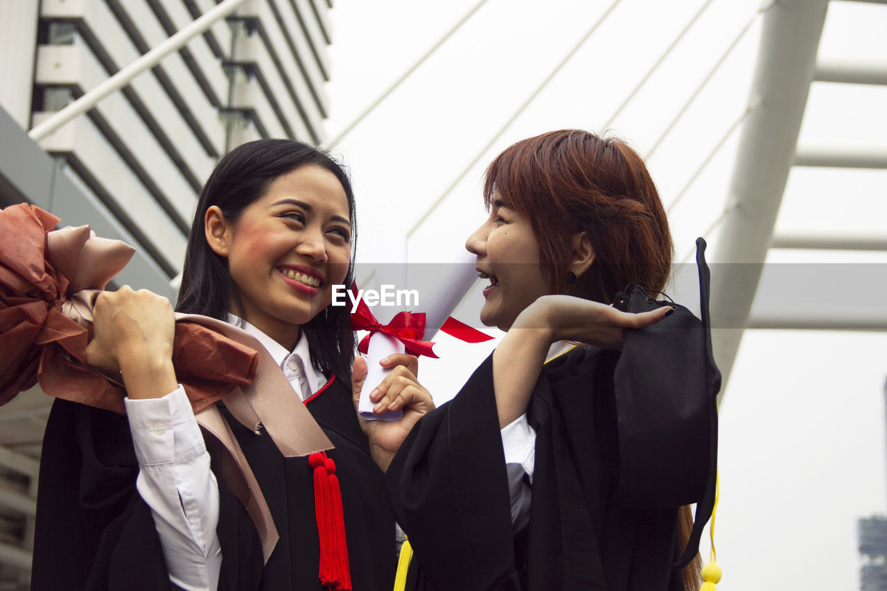Smiling female friends wearing graduation gowns