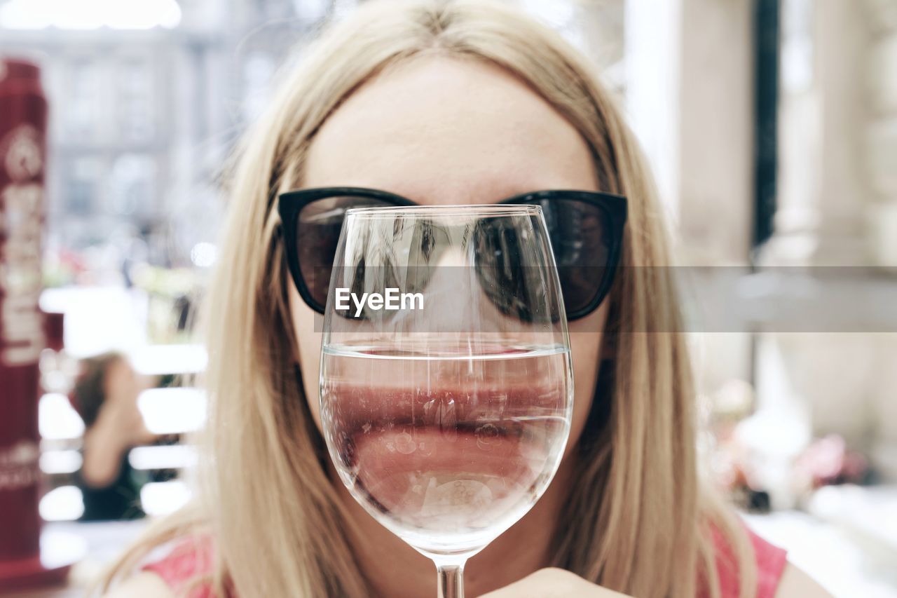 Close-up portrait of woman covering face with wineglass outdoors