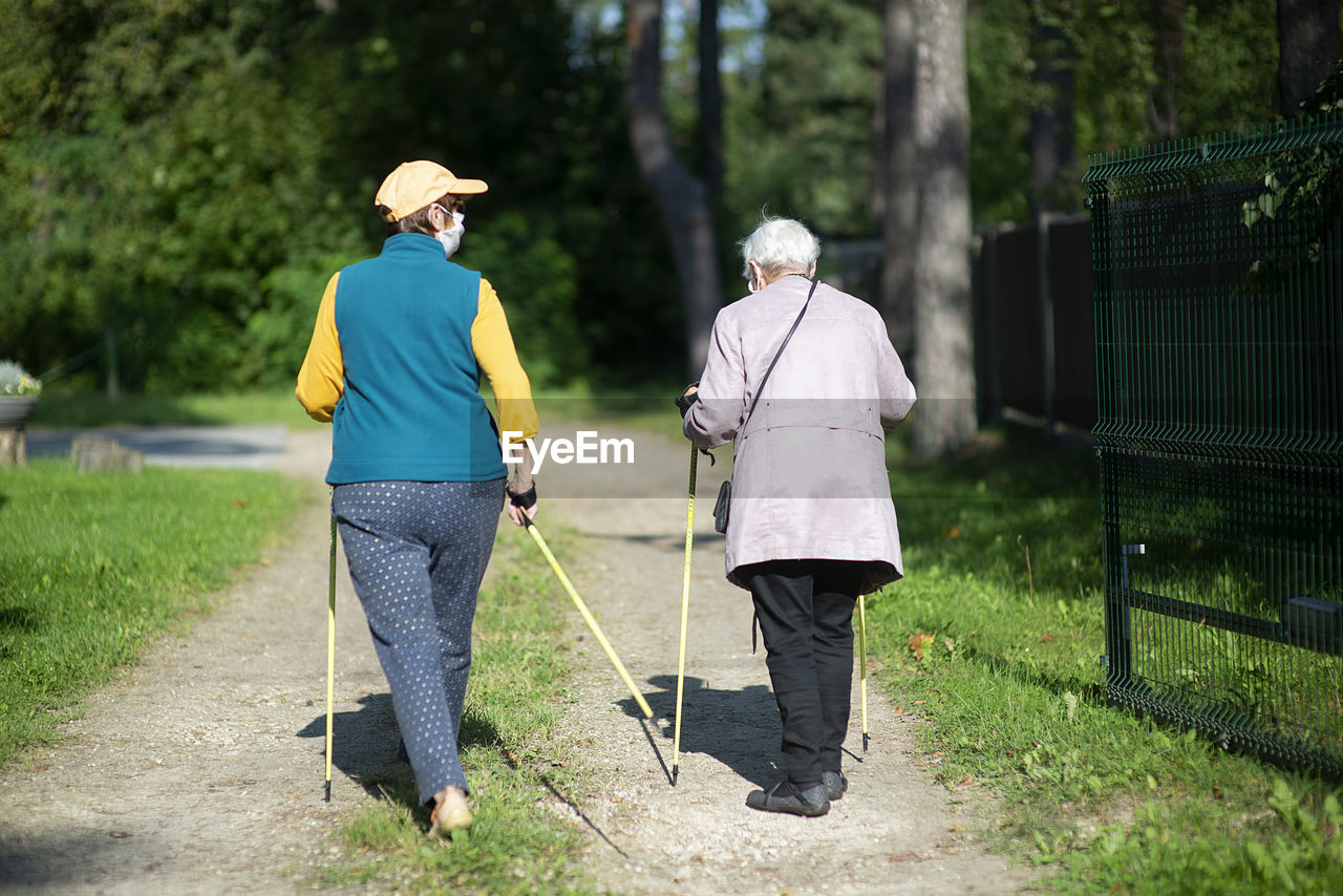 Rear view of two senior women with face masks  nordic walking poles during covid-19 pandemic