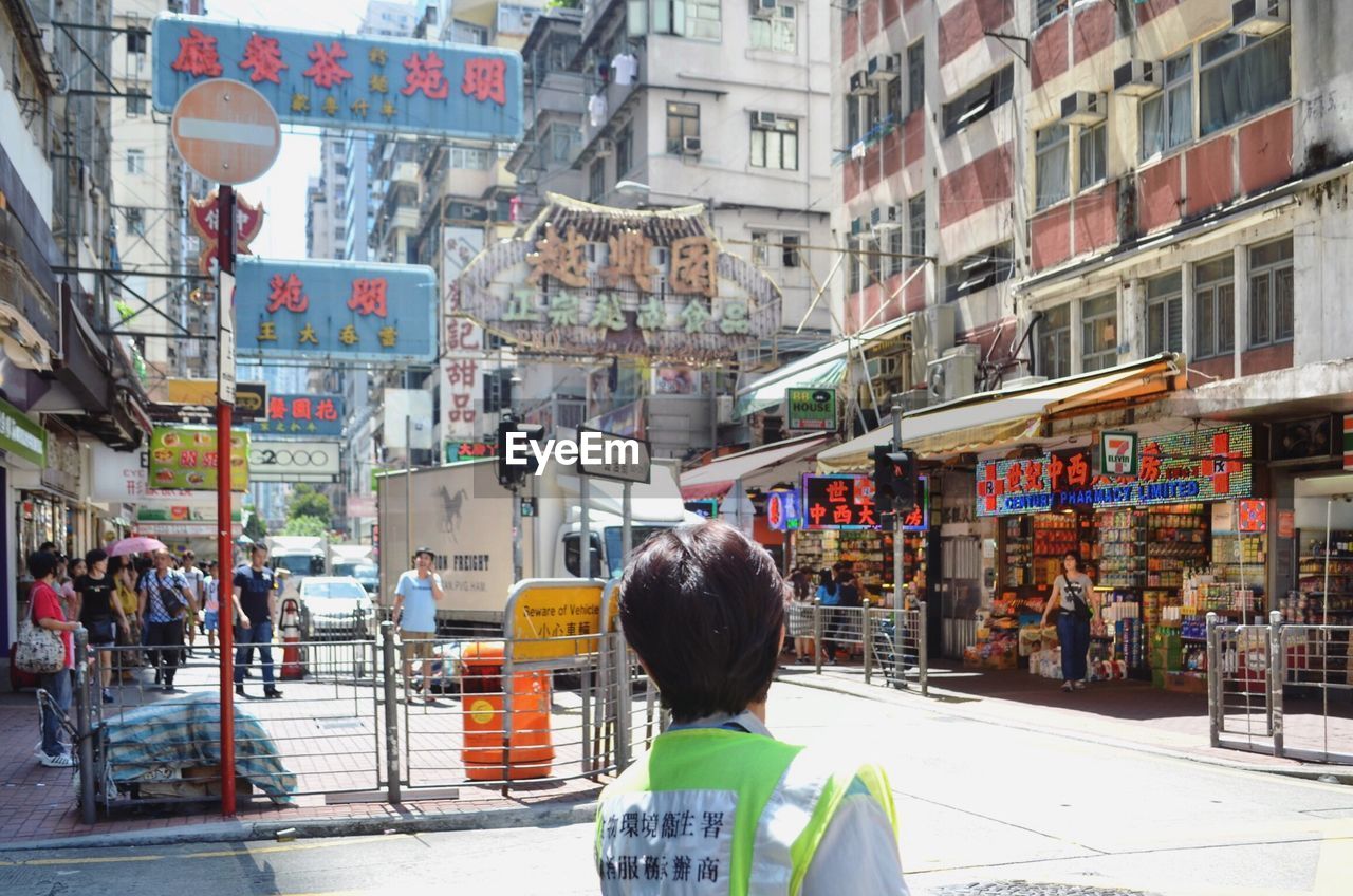 REAR VIEW OF PEOPLE WALKING ON CITY STREET