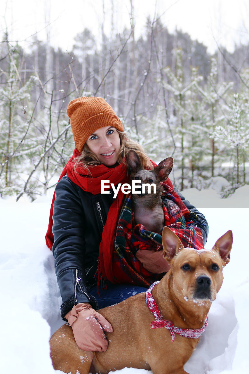 Beautiful smiling woman is on a walk with her two dogs in winter coniferous forest.