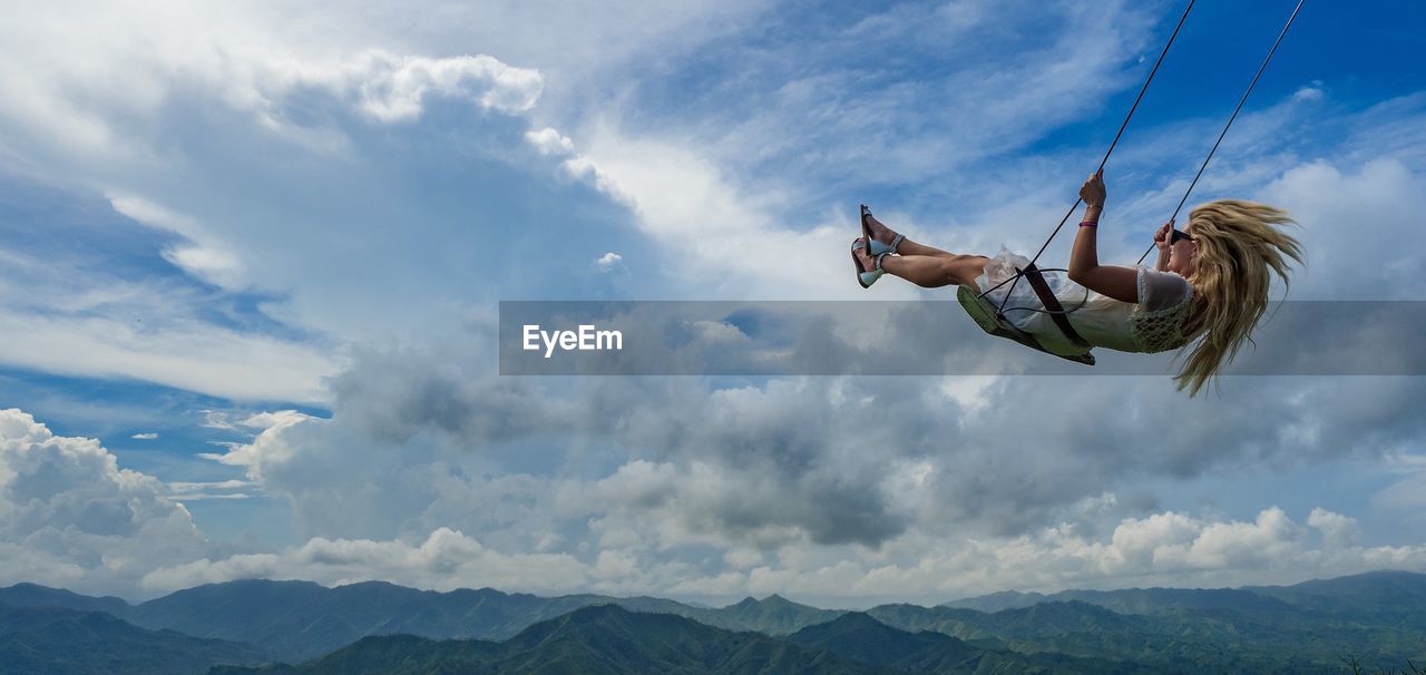 Side view of woman swinging against landscape and sky