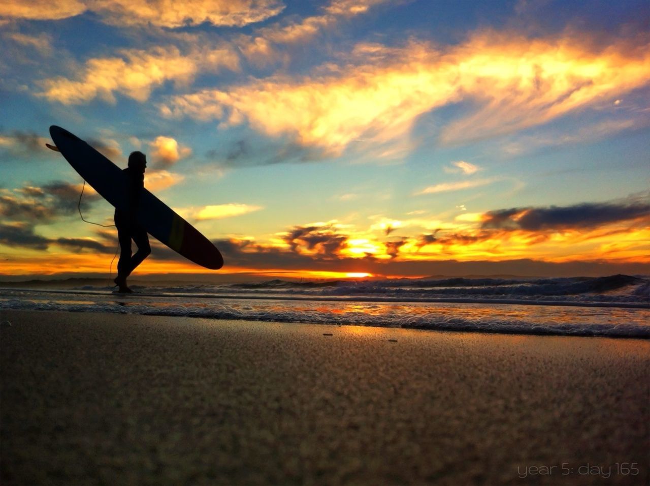 Silhouette man with surfboard at beach against sky during sunset