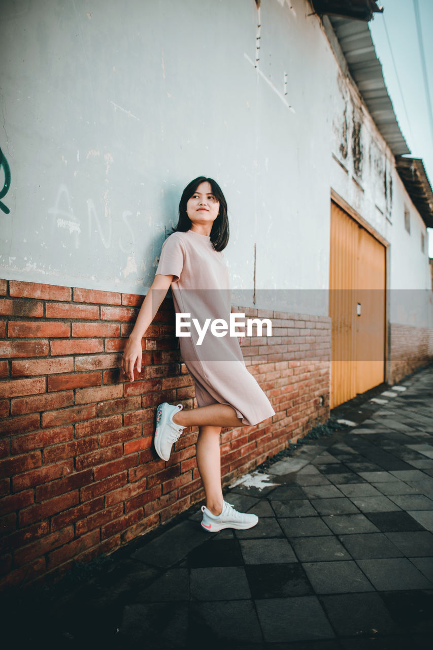 A short hair asian woman in casual clothes is smiling and leaning against the wall