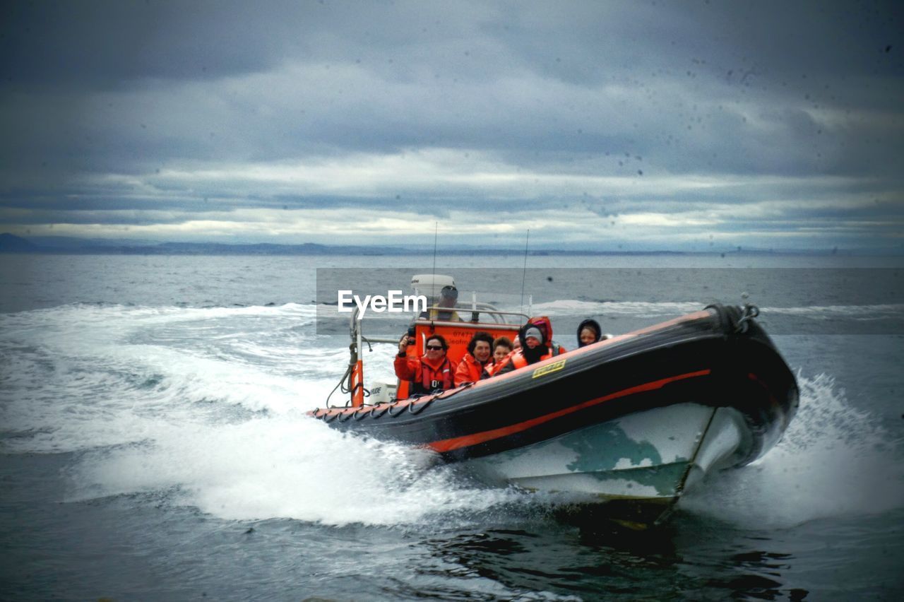 People enjoying in motorboat on sea against cloudy sky