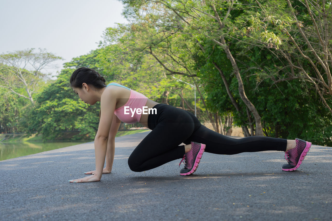 Full length of young woman exercising on road by river at park