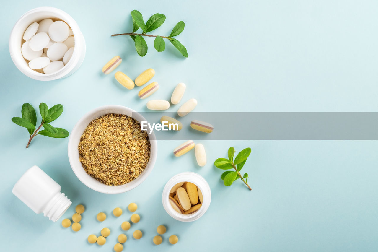 Vitamins and herbal supplements in jars with a green plant.