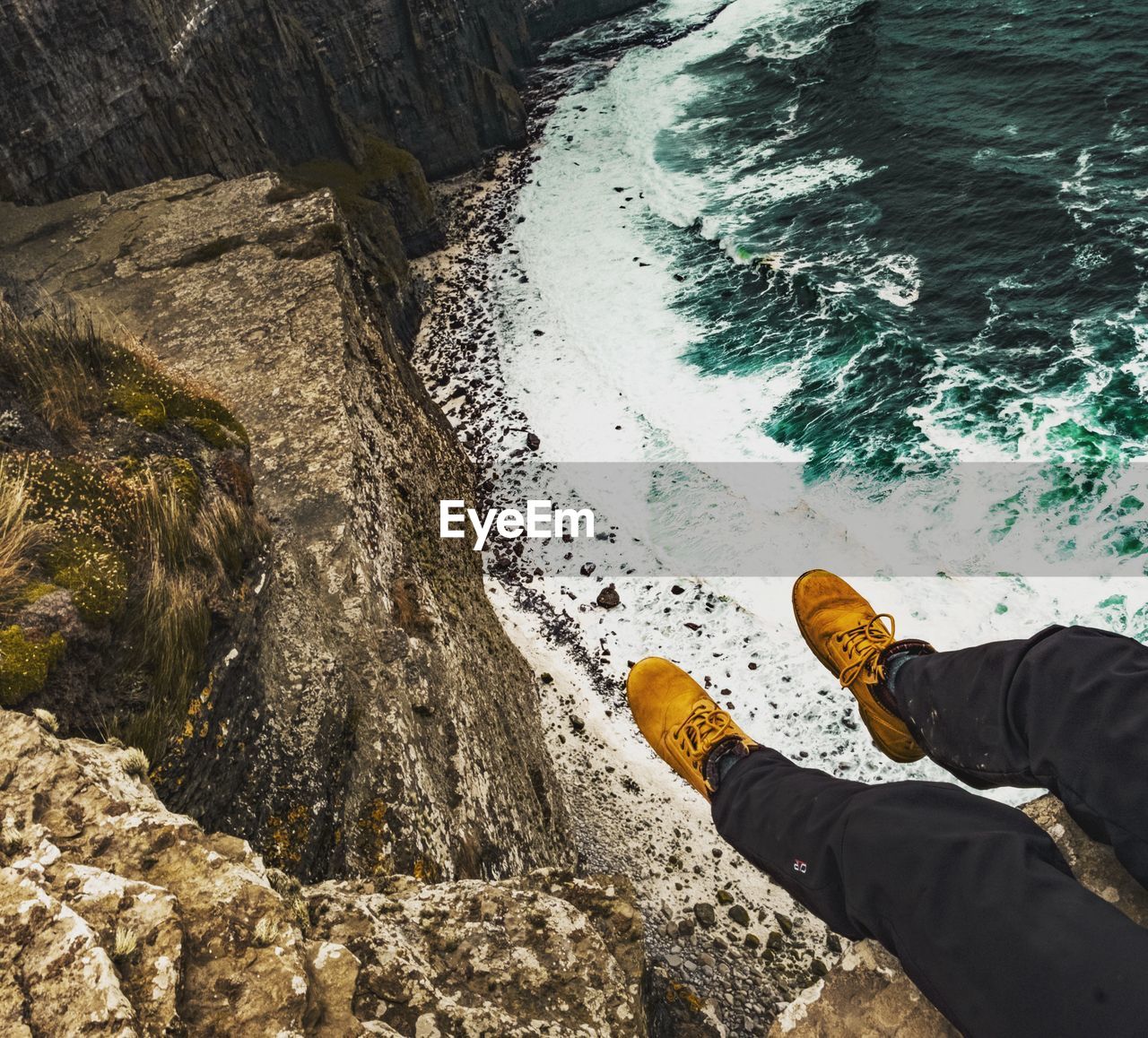 LOW SECTION OF PERSON ON ROCK AT SEA SHORE