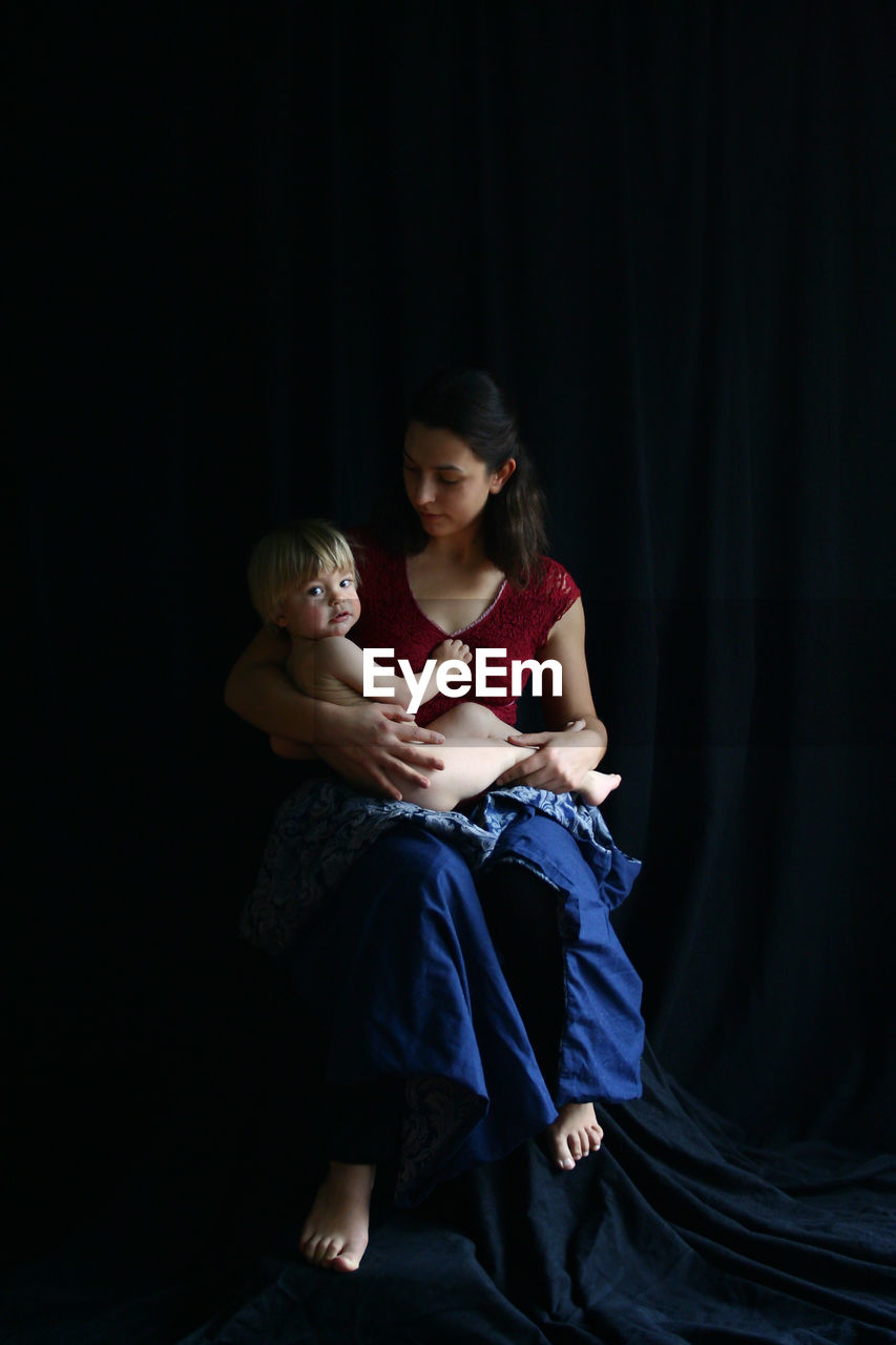 Full length of young woman with son sitting on black textile