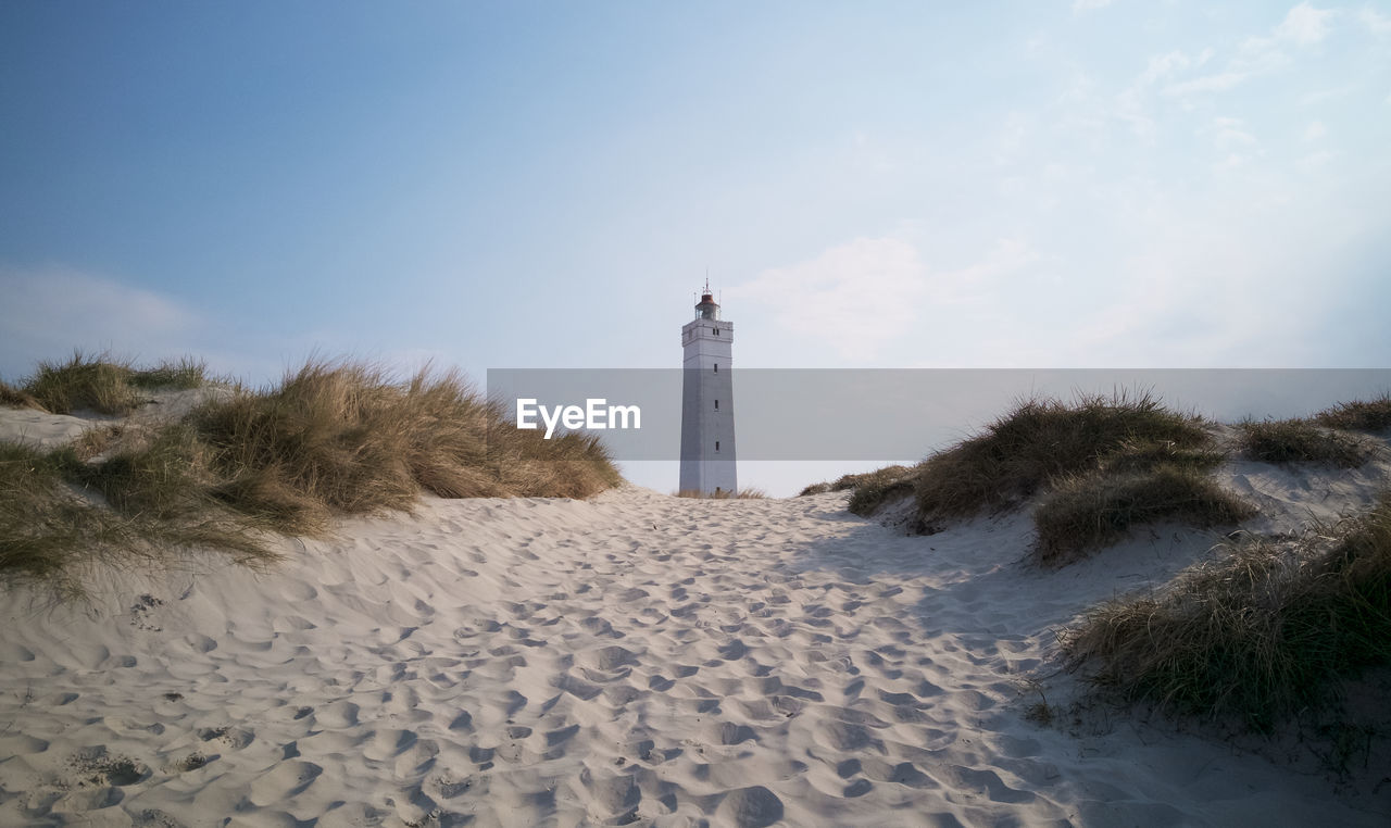 Lighthouse on beach against sky