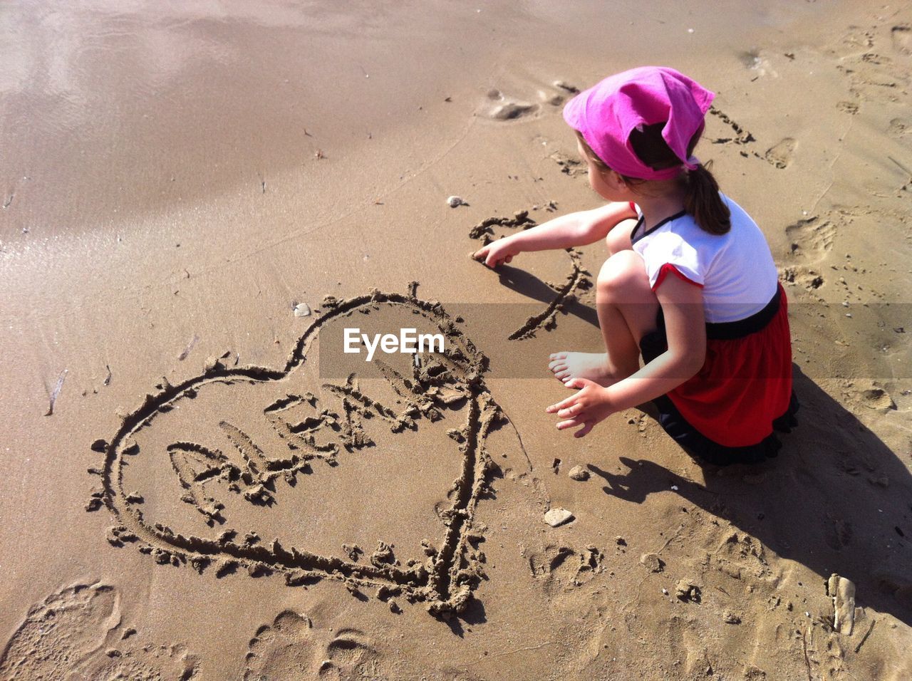 High angle view of girl writing in sand on shore at beach during summer